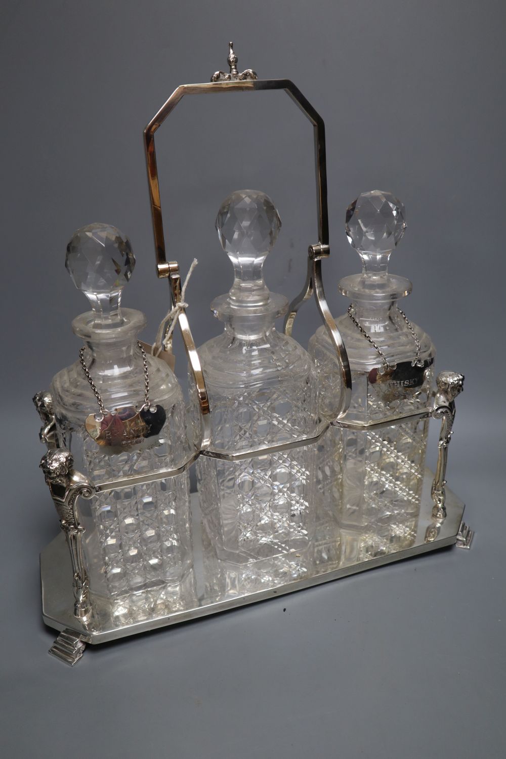 An Edwardian plated decanter stand, fitted three square cut glass decanters and three silver bottle labels, 36cm wide